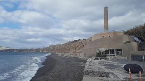 A coastal building with a tall chimney, a beach, and a rocky cliff.