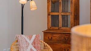 Ein gemütliches Zimmer mit einem Korbssessel, einem Holzschrank und einer Stehlampe.