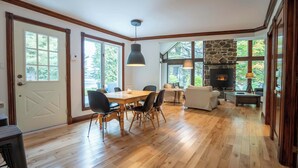 A spacious living area with a stone fireplace, wooden flooring, and large windows offering a view of the outdoors. - Lakefront | Quai 948 (Lac-Drolet)
