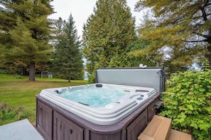 Un jacuzzi en un patio trasero con terraza de madera, rodeado de árboles y césped.