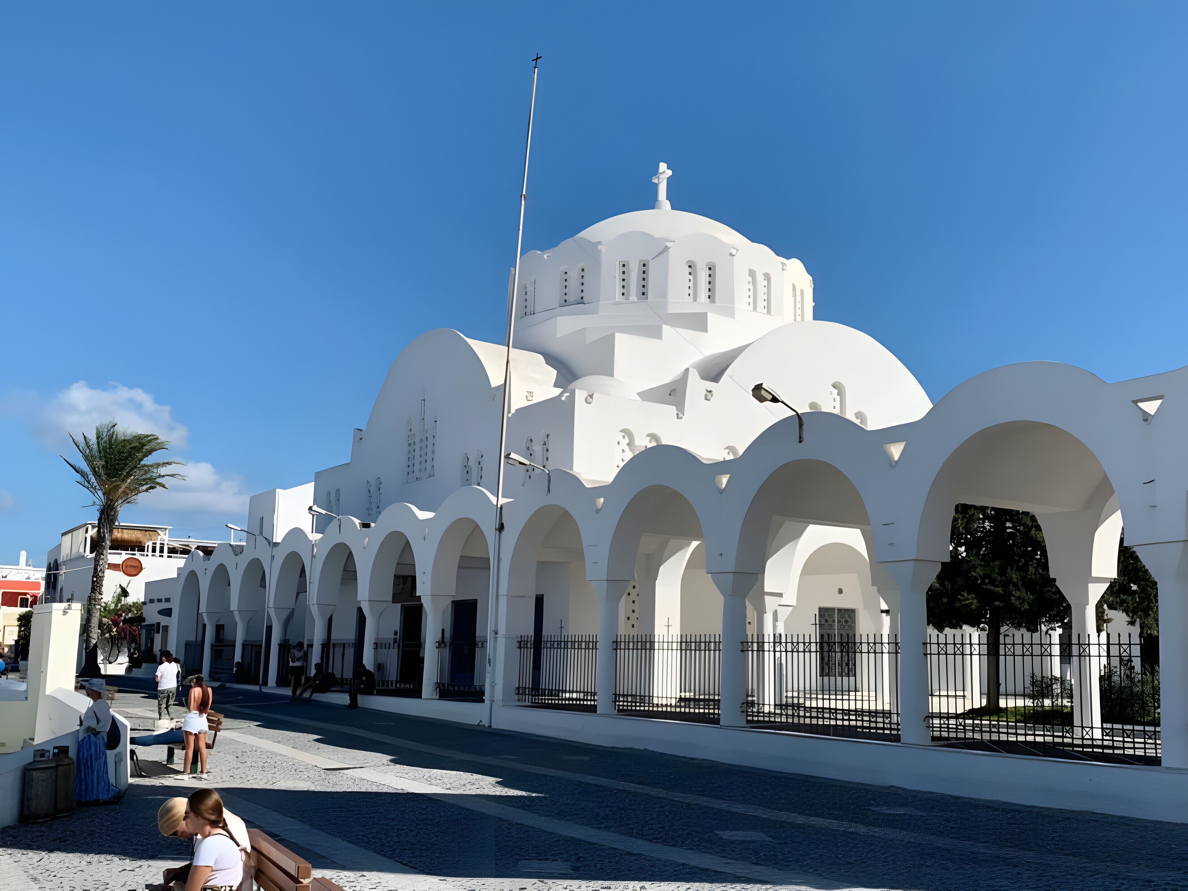 A white building with multiple arches and a dome, a flagpole, and a clear blue sky.