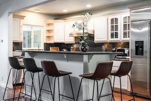 A modern kitchen with white cabinetry, a central island with bar stools, and stainless steel appliances. - Spacious Family Retreat in San Dimas Great Location (Covina)