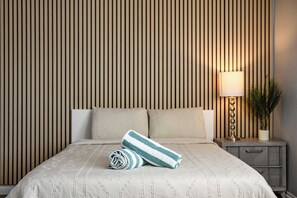 A neatly made bed with a striped towel and a rolled-up towel, a bedside lamp, and a potted plant on a nightstand. - Spacious Family Retreat in San Dimas Great Location (Covina)