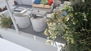 Een terras met buitenmeubilair, planten in potten en een witte omheining.