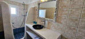 A bathroom with a shower, a sink with a basin, a mirror, and a window.