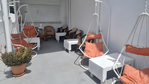 A covered outdoor seating area with white wicker furniture, orange cushions, and a potted plant.