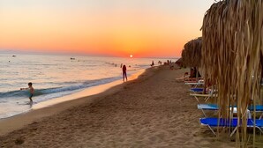 A beach with a sunset, people, and beach chairs.