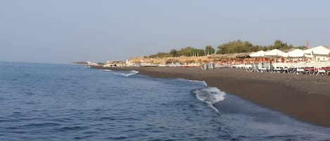 A beach with umbrellas and lounge chairs, a clear sky, and calm sea.