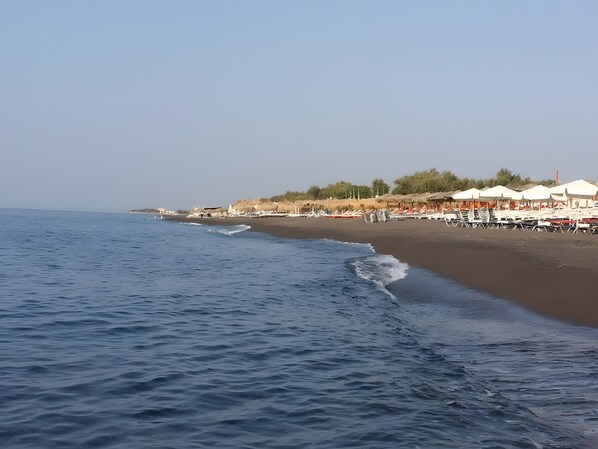 A beach with umbrellas and lounge chairs, a clear sky, and calm sea.
