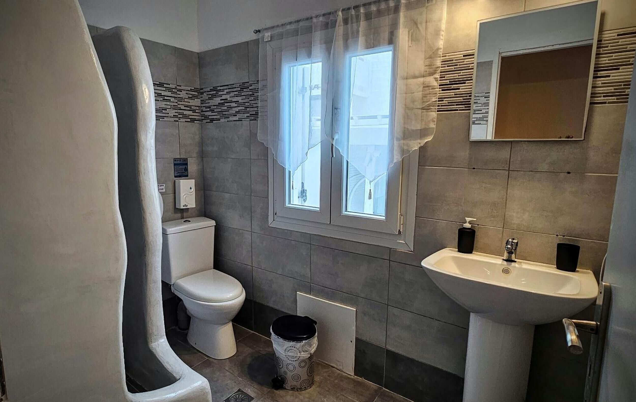 Un baño con inodoro, lavabo y ventana con cortinas.