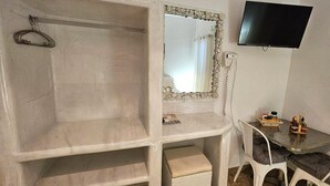 A bathroom with a shower, a mirror, a television, and a small table with toiletries.