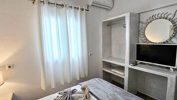 A bathroom with a shower curtain, a vanity with a mirror, a television, and a towel rack.