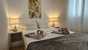 Quarto de hotel com uma cama, duas luminárias de cabeceira, um quadro na parede e uma janela com cortinas.