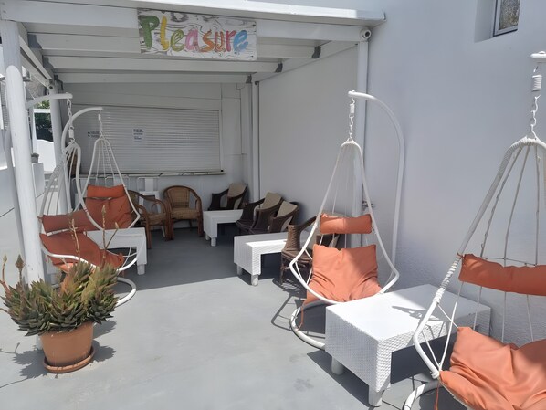 A covered outdoor seating area with white wicker furniture, orange cushions, and a potted plant.