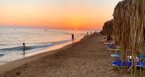 A beach with a sunset, people, and beach chairs.