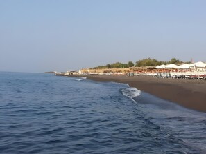 A beach with umbrellas and lounge chairs, a clear sky, and calm sea. - Studio Apartment 'Pleasure View 1  Persons 3' with Mountain View, Wi-Fi and Air Conditioning (Perissa)