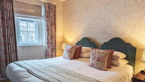 A neatly made bed with floral-patterned pillows, a green headboard, and a window with curtains. - Three Salmons Hotel (Usk)