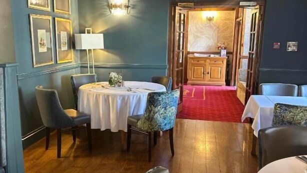 A dining area with tables and chairs, framed pictures on the wall, and a red carpet leading to another room. - Three Salmons Hotel (Usk)