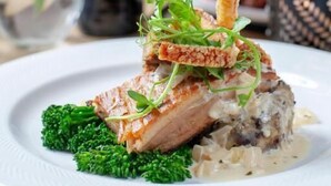 A plate of food with a piece of meat, greens, and a sauce, accompanied by a bottle of wine and a glass. - Three Salmons Hotel (Usk)