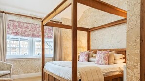 A four-poster bed with a wooden frame and white bedding, a chair with floral upholstery, and a window with patterned curtains. - Three Salmons Hotel (Usk)