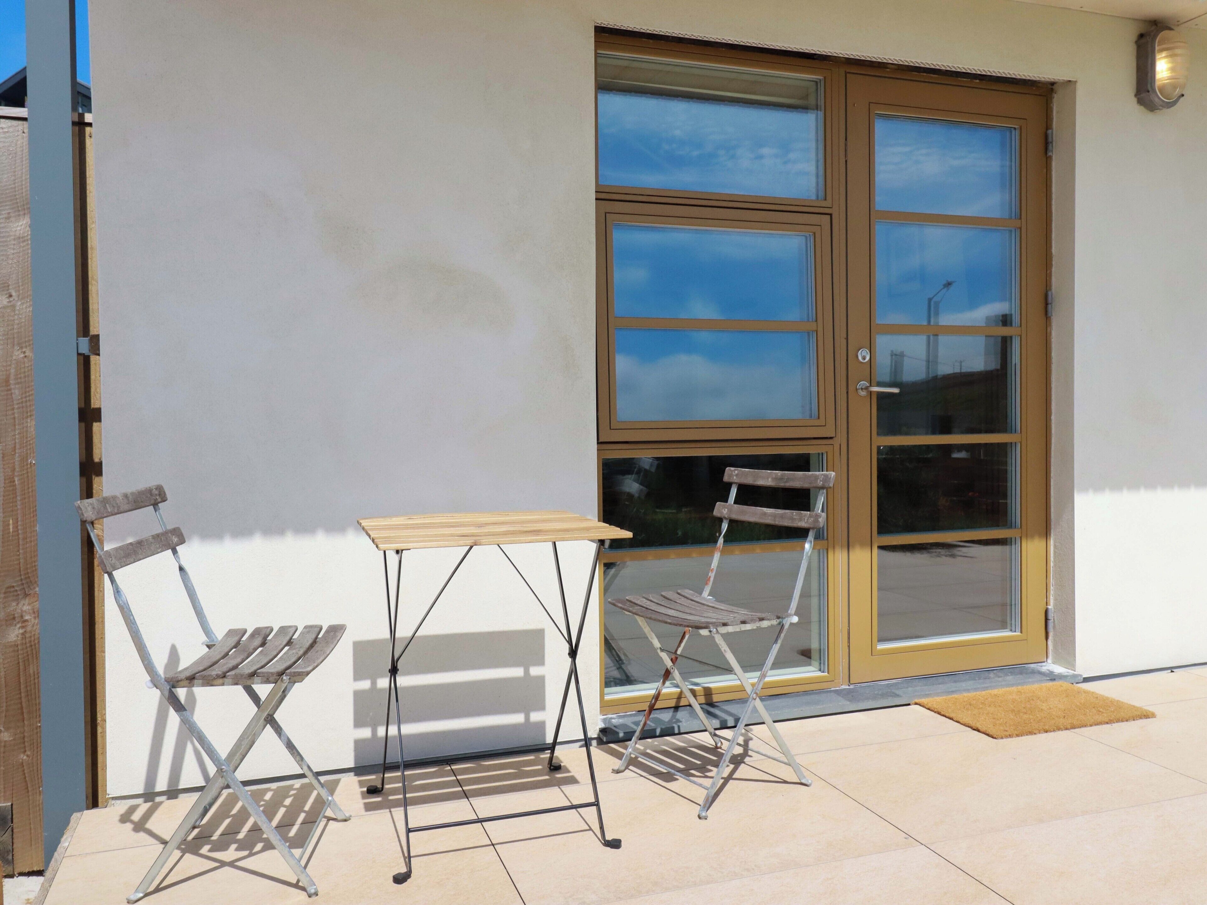 Une terrasse avec deux chaises en métal et une petite table, une porte en bois et une fenêtre.