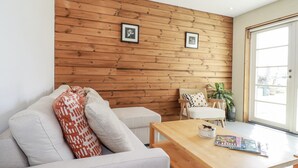 Una sala moderna con una pared de madera, un sofá con cojines estampados, una mesa de centro de madera y un sillón con un cojín estampado.