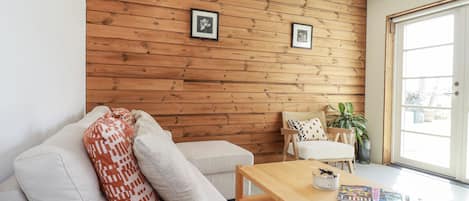 Uma sala de estar moderna com parede de madeira, um sofá com almofadas estampadas, uma mesa de centro de madeira e uma poltrona com almofada estampada.
