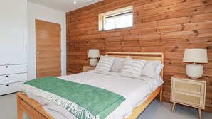 Un dormitorio con pared de madera, una cama con ropa de cama blanca, dos mesitas de noche con lámparas y un armario.