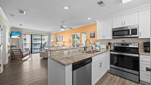 A modern kitchen with white cabinets, granite countertops, a built-in dishwasher, a microwave, an oven, and a coffee maker. - Romar Beach 208 Steps from the Gulf! (Orange Beach)