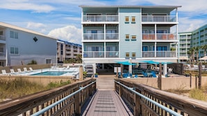 A multi-story hotel with a pool area, outdoor seating, and a wooden boardwalk leading to the entrance. - Romar Beach 208 Steps from the Gulf! (Orange Beach)