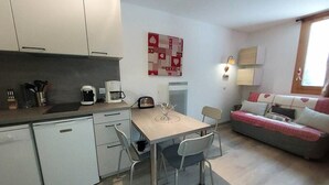 Eine kleine Küche mit Kaffeemaschine, Toaster und Spüle. Ein Esstisch mit Stühlen und eine Couch mit herzförmigen Kissen.