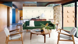 A modern living room with a green sofa, wooden chairs, a coffee table, and a view of a garden through large windows. - The Desert Wave Midcentury Design in Palm Desert (Palm Desert)