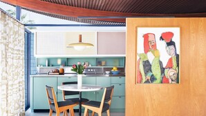 A modern kitchen with teal cabinets, a white dining table, and chairs. There is a painting on the wall and a hanging light fixture above the counter. - The Desert Wave Midcentury Design in Palm Desert (Palm Desert)