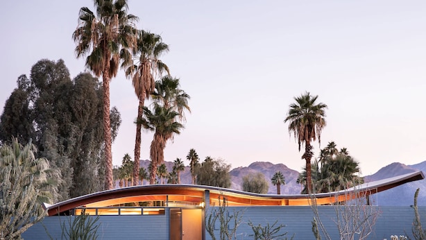 A modern building with a curved roof, surrounded by desert vegetation and palm trees. - The Desert Wave Midcentury Design in Palm Desert (Palm Desert)