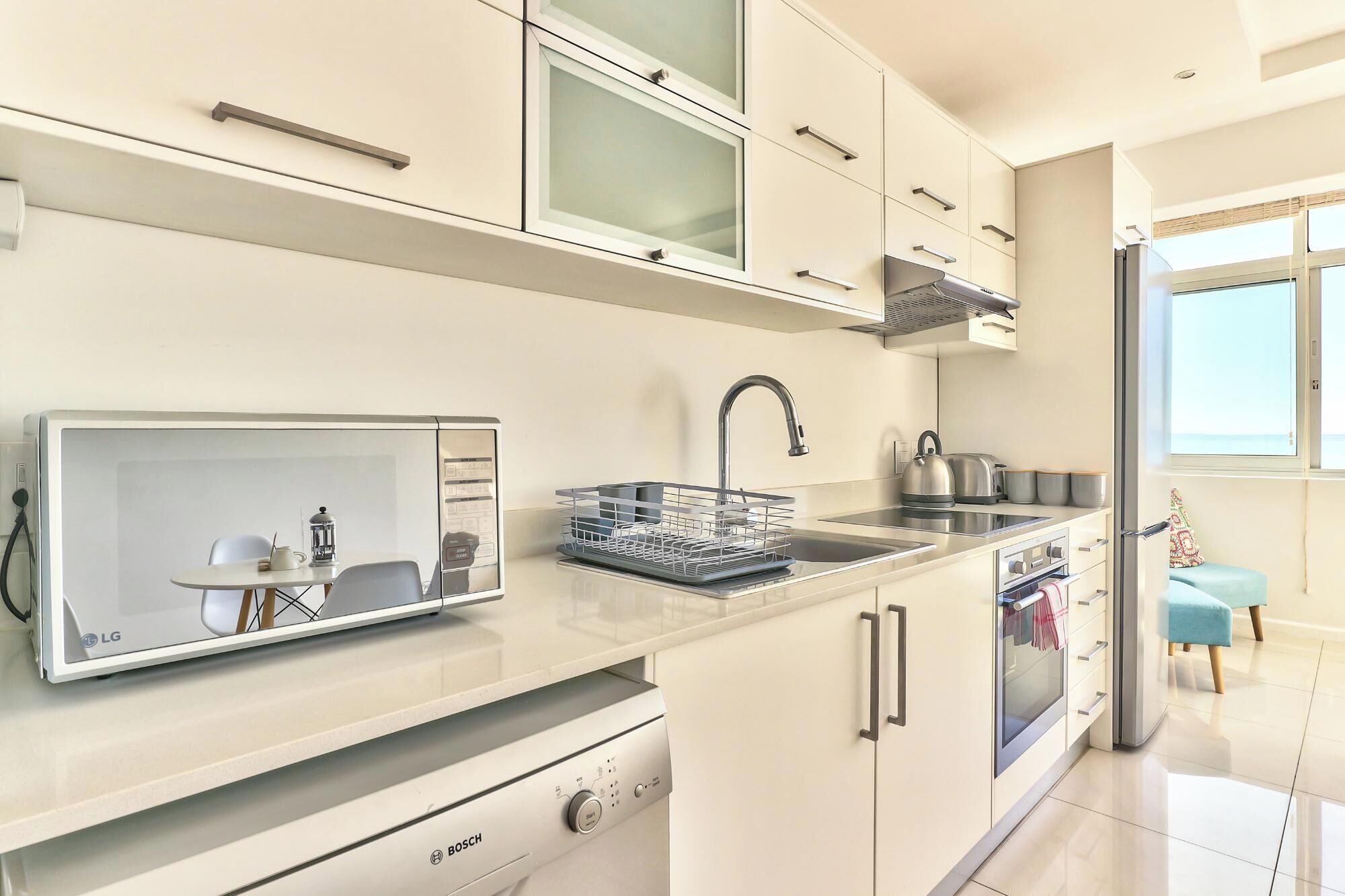 A modern kitchen with a Bosch stove, a sink, and a window overlooking a balcony.