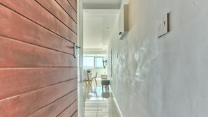 Un couloir avec un mur en bois, un sol carrelé de carreaux blancs et une vue sur un coin repas avec des chaises et une table.
