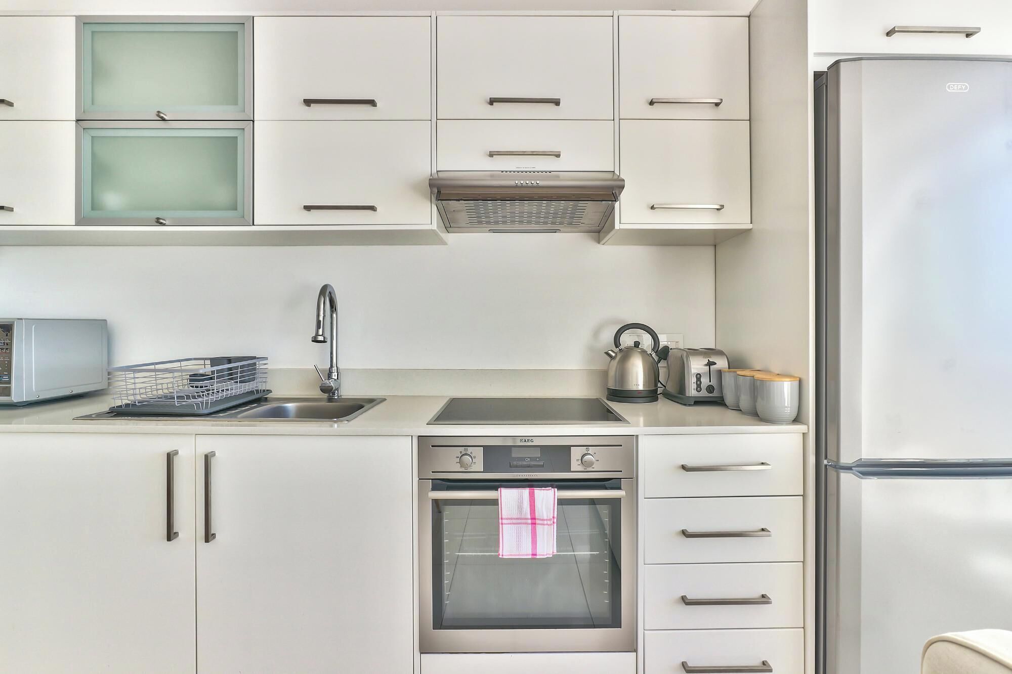 A modern kitchen with white cabinets, a built-in oven, a microwave, a kettle, and a toaster.