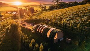 A cylindrical, vine-covered structure with a small attached building, surrounded by a rural landscape with fields and trees, during sunset. - Refúgio Vista da Montanha (Imaruí)