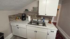 A small kitchen with white cabinets, a marble countertop, a coffee maker, a sink, and a small plant. - Cozy 1-bed, 1-bath apartment in Geneva, NY, steps from downtown & Seneca Lake! (Geneva)