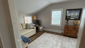 A cozy living room with a beige sofa, a patterned rug, a wooden cabinet, and a framed picture on the wall. - Cozy 1-bed, 1-bath apartment in Geneva, NY, steps from downtown & Seneca Lake! (Geneva)