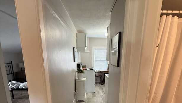 A narrow hallway with a red carpet leading to a kitchen area with white cabinets and a window with blinds. - Cozy 1-bed, 1-bath apartment in Geneva, NY, steps from downtown & Seneca Lake! (Geneva)
