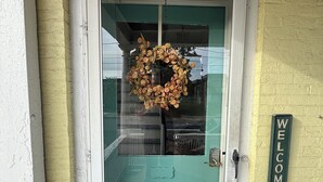A turquoise door with a wreath, a 'WELCOME' sign, and a white porch railing. - Cozy 1-bed, 1-bath apartment in Geneva, NY, steps from downtown & Seneca Lake! (Geneva)
