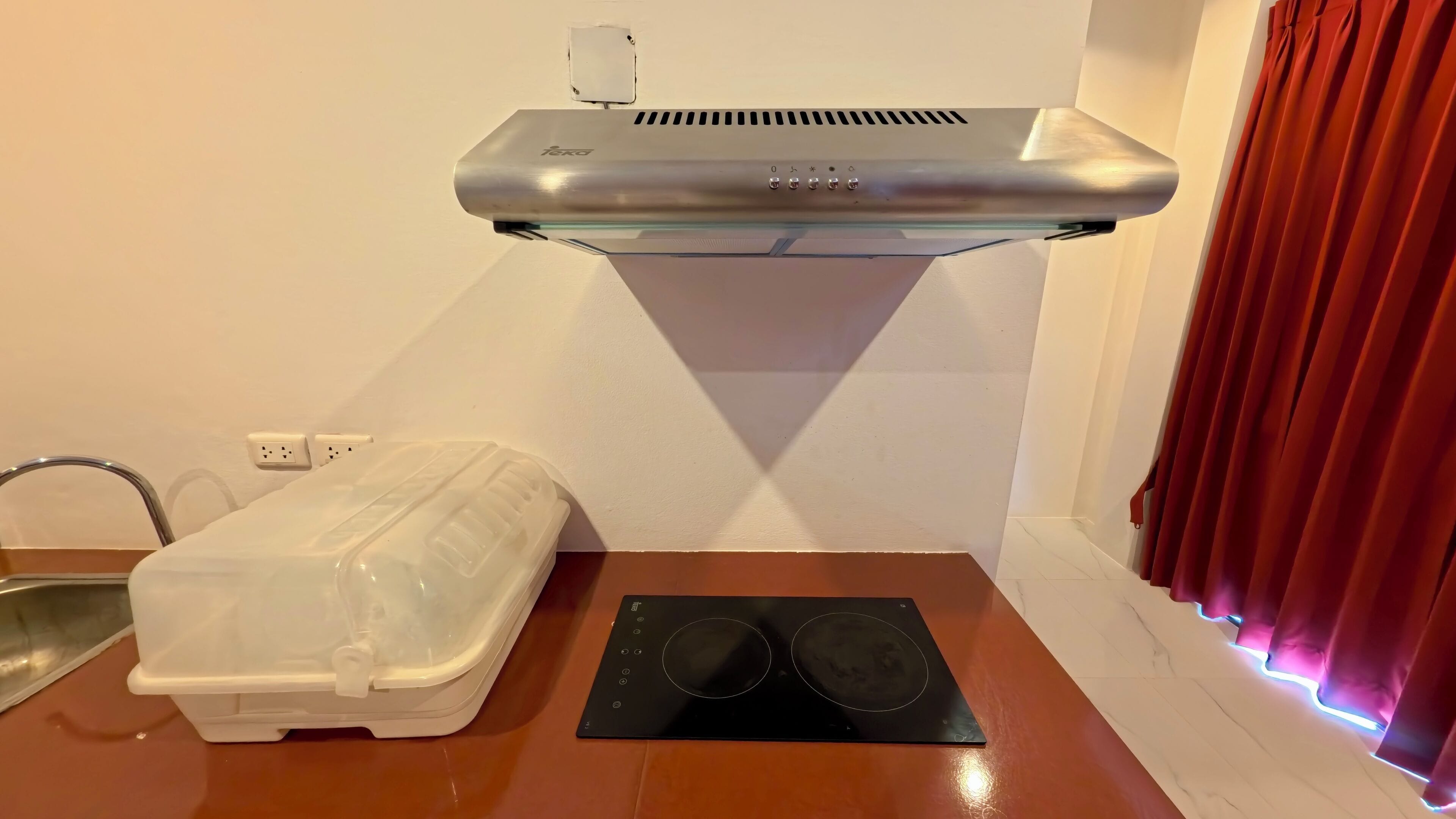Una cocina con campana de acero inoxidable, encimera blanca, placa de inducción negra y un recipiente de plástico blanco.