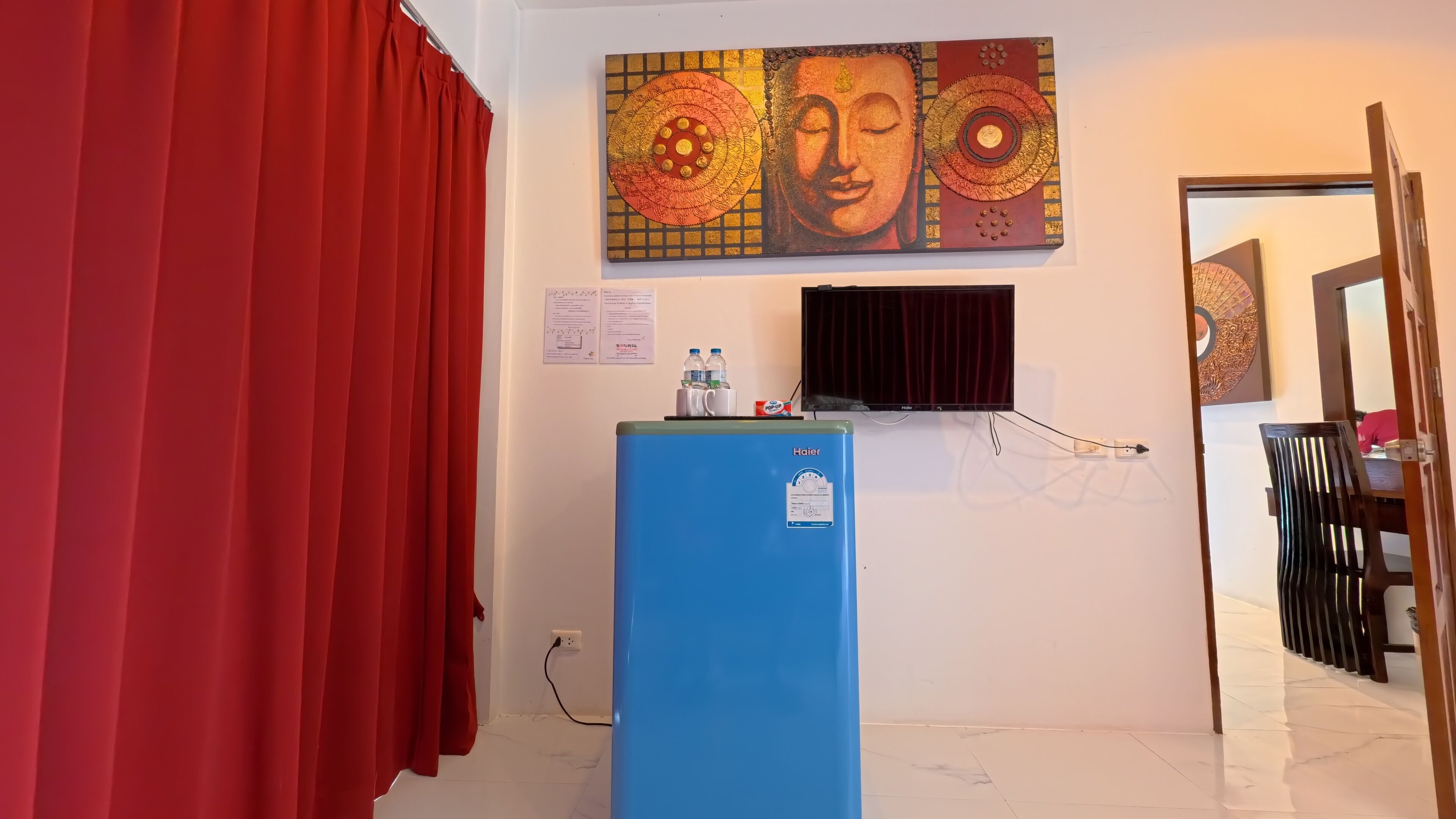 A room with a blue refrigerator, a flat-screen TV, and a red curtain.