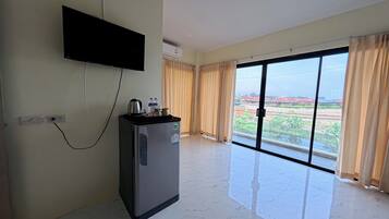 Habitación de hotel con televisión de pantalla plana en la pared, refrigerador con bebidas y un gran ventanal corredero que da a un espacio exterior.