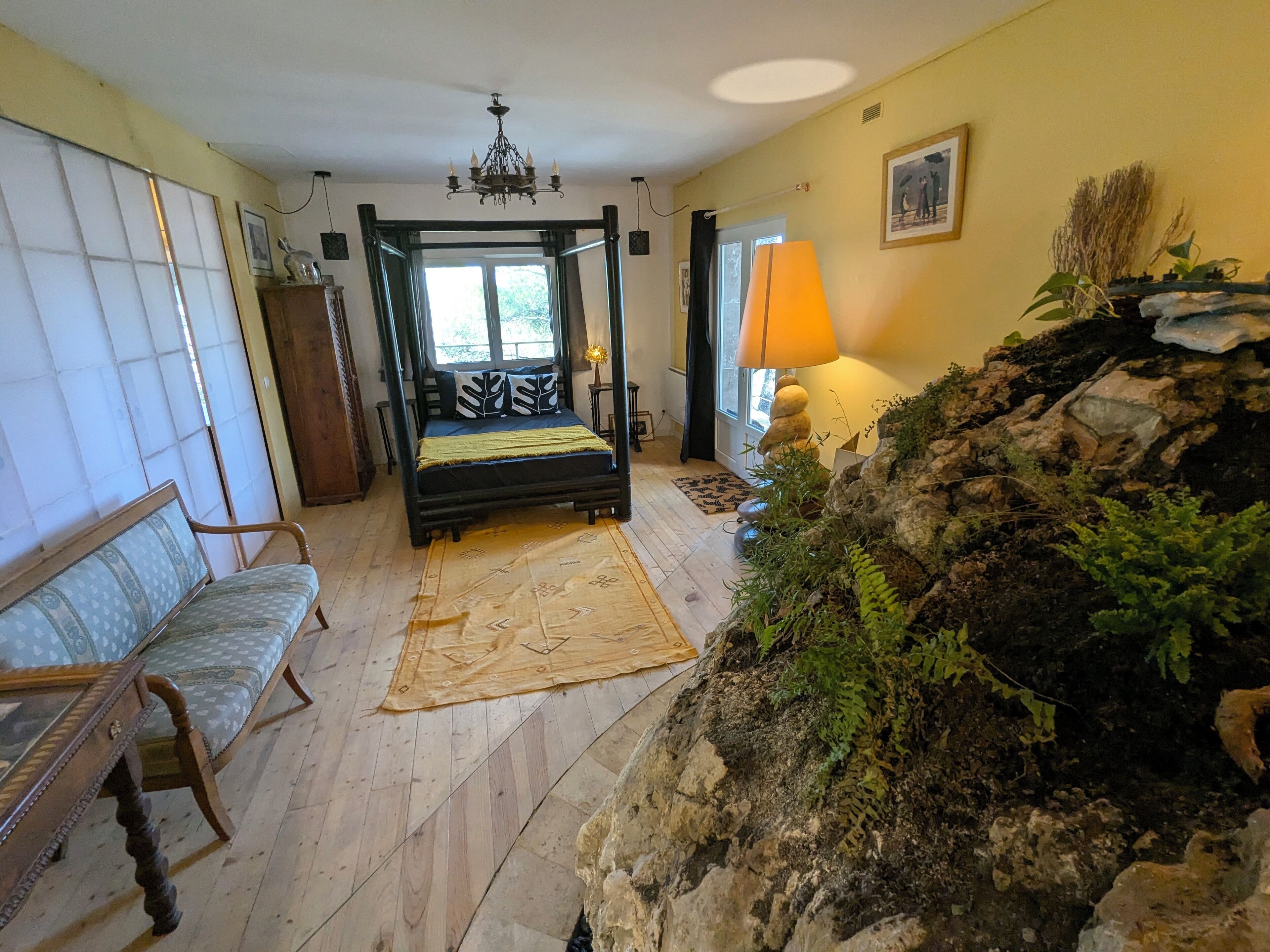 A room with a four-poster bed, a bench, a lamp, and a rock garden.