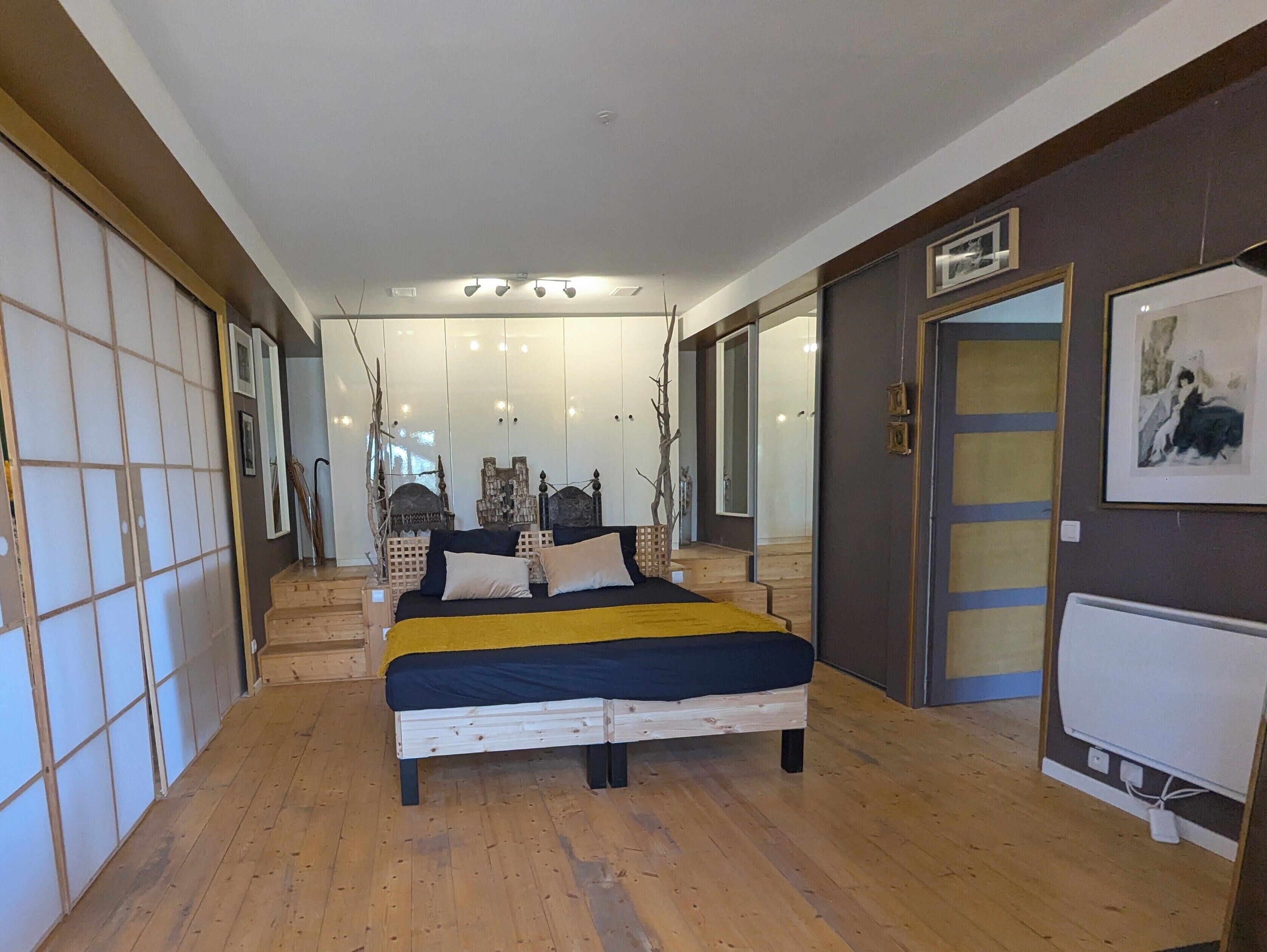 A bedroom with a bed, wooden flooring, a mirror, and a door with a picture frame.