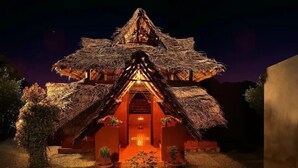 Un edificio con tetto di paglia e una zona centrale illuminata, circondato da piante in vaso.