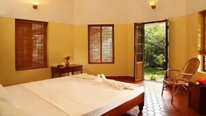 Una camera da letto con un letto, due finestre, una porta che dà su un giardino e una sedia.