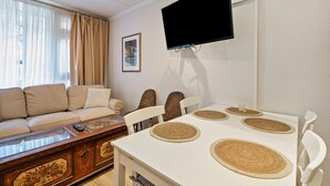 Un soggiorno con divano, tavolino, televisore a parete e tavolo da pranzo con sottopiatti.